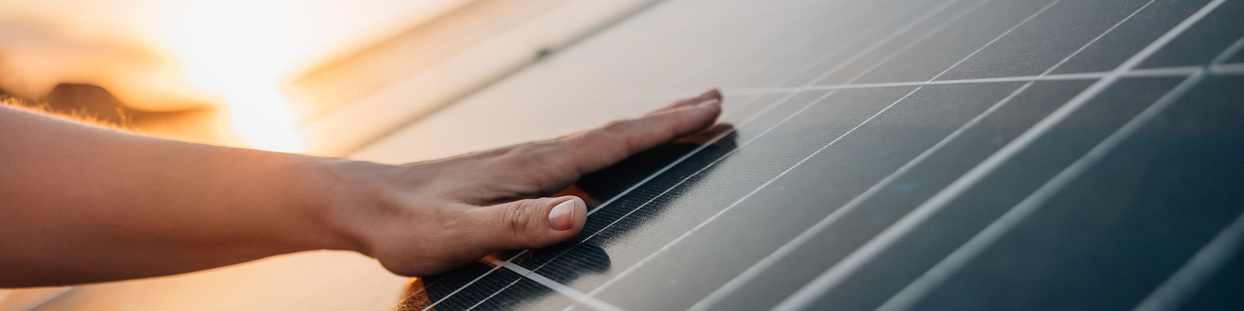 Nachhaltige Energie im Fokus Hand berührt ein Solarmodul bei Sonnenuntergang – Symbol für nachhaltige Energie und Photovoltaik-Technologie.